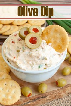 a white bowl filled with dip surrounded by crackers and olives