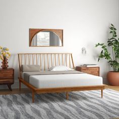 a bed sitting on top of a wooden floor next to a mirror and plant in a room