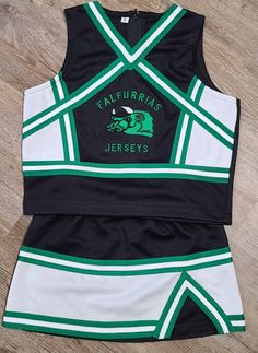 a black and white cheer uniform with green lettering on the front, sitting on a wooden floor