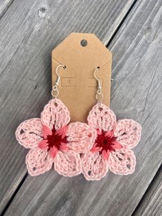 pink crochet flower earrings with silver hooks on wooden table next to brown tag