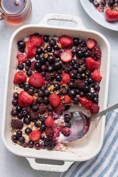 berries, blueberries and other fruit are in a casserole dish with a spoon