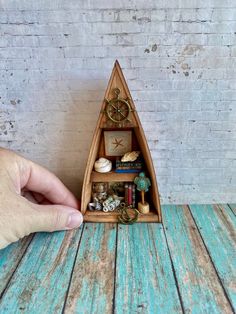 a small wooden boat shaped shelf with various items in it and a hand reaching for the top