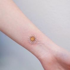 a small daisy tattoo on the left inner arm, with a yellow dot in the middle