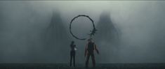 two people standing in front of a giant circular object on a foggy day,