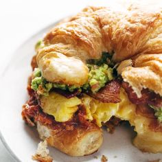 a croissant sandwich with bacon, eggs and avocado on it sitting on a plate