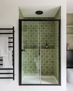 a bathroom with green and white tiles on the wall, shower stall and towel rack