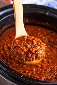 a spoon full of chili and beans in a slow cooker with a wooden ladle