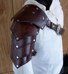 a person wearing a brown leather armor on their arm and shoulder with metal rivets