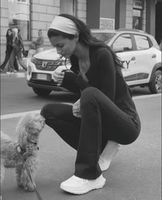 a woman kneeling down next to a small dog on a leash and petting it