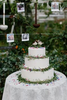 a three tiered cake with flowers and greenery on the top is sitting on a table