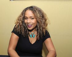 a woman with curly hair sitting in front of a table and looking at the camera