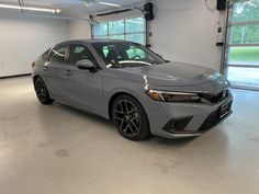 a grey car parked in a garage next to two large windowed windows on the wall