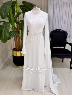 a white wedding dress on display in front of a potted plant and black chair