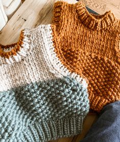 three knitted sweaters sitting on top of a wooden floor next to each other