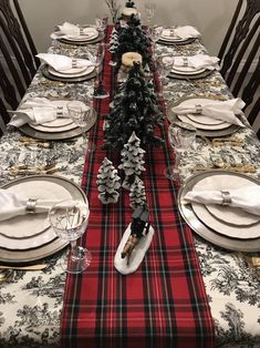 the table is set for christmas dinner with white plates and silverware, black and red plaid runner