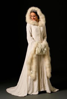 a woman in a white gown and fur collar standing with her hands on her hips