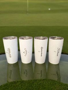 four white cups sitting on top of a glass table in front of a green golf course