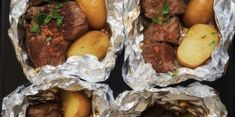 four pieces of tin foil with meat and potatoes in them on a black table top