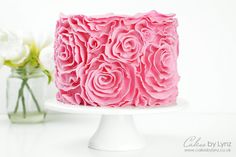 a pink frosted cake sitting on top of a white plate next to some flowers