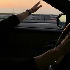 a person driving a car with their hand on the steering wheel while holding something up in front of them