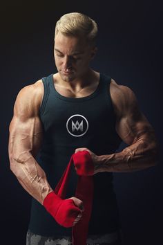 a man in a black tank top is holding a pair of red gloves and looking down at his arm