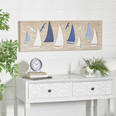 a white table topped with a clock next to a potted plant and wall hanging