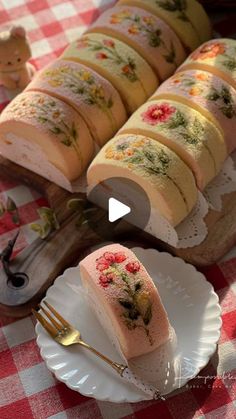 a table topped with lots of cakes on top of white plates and silverware next to a red checkered table cloth