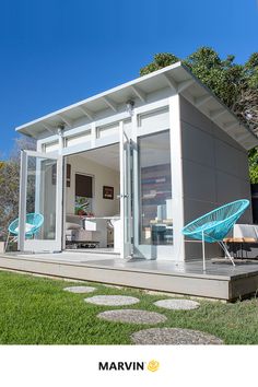 a small white house sitting on top of a lush green field next to a blue lawn chair