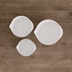 three white dishes sitting on top of a wooden table