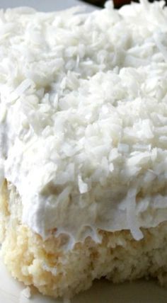 a piece of cake with white frosting and coconut on top sitting on a plate