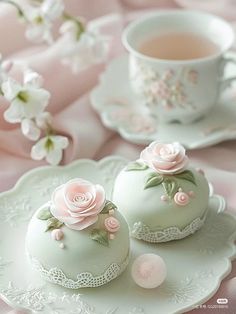 two green tea cakes with pink roses on them sitting on a plate next to a cup and saucer