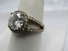 Vintage Sterling CZ Rhinestone Ring, Sz. 10.5.  The main stone is clear with nice sparkle and is appx. 10mm round.  It is set with four prongs.  It has a halo of 1mm clear rhinestones that also goes half way  down in the band in an open v split band.  The band is appx. 8mm wide and tapers to 2.5mm at the back of the finger.  This tests as sterling and is marked sterling with an appx weight of 9.12 gr.  Very good condition other than oxidation that will polish away.  It is not signed by the maker.  Age is estimated at 1980's-1990's.  (W121722.1X1 Ss9477 J LD 2/5/23) (JK 6.9.2024) You can search me at my own store: mariasvintage.com and also I have an etsy store at mariasvintage2.com or on pinterest under pinterest.com/mariasvinta0654/ where I have most of my items for sale across all my ven Brilliant Cut Diamond Ring For Party, Party Diamond Ring With Accents, Party Diamond Ring With Halo Setting, Halo Setting Round Party Rings, Party Diamond Ring With Center Stone, Party Diamond White Diamond Ring, Round Crystal Ring With Prong Setting For Party, Party Rings With Center Stone And Round Shape, Party Rings With Center Stone