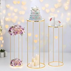 three gold stands with candles and flowers on them in front of a white background filled with lights