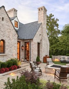 an outdoor living area with chairs and fire pit in front of a brick house at dusk