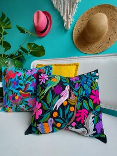 three colorful pillows on a white couch with hats and plants in the corner behind them