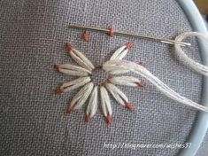 an embroidery project with white and red flowers on grey fabric, next to a needle