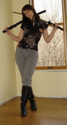 a woman holding two swords in her hands and standing on a hard wood floor next to a window