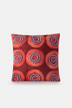 an orange and purple pillow with circular designs on the front, sitting on a white surface