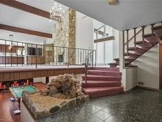 a living room filled with furniture and a fire place next to a stair case in front of a stone fireplace