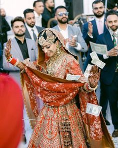 a woman in a red and gold wedding dress is holding her hands out to the crowd