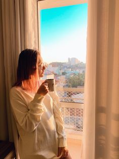 a woman sitting in front of a window drinking from a cup