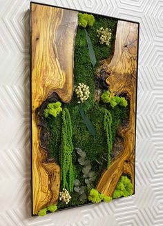 an art piece made out of wood with moss and flowers in the center is mounted on a wall