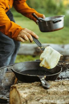 a man is cooking food over an open fire with a skillet in the foreground