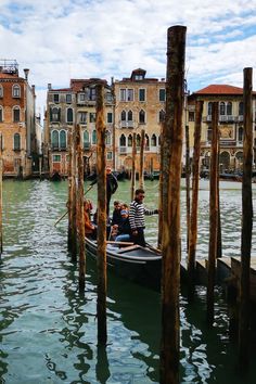 two people in a gondola on the water next to some poles and buildings