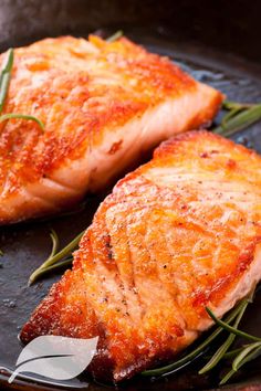 two pieces of salmon on a pan with rosemary