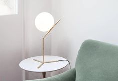 a white table with a green chair and a round light on the end, in front of a white wall