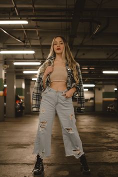 a woman standing in an empty parking garage wearing ripped jeans and a cropped top