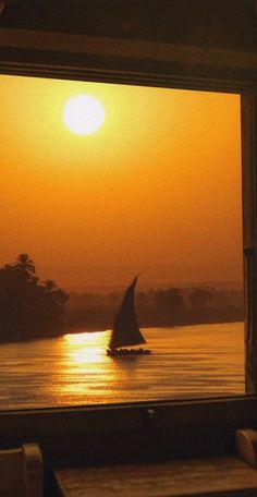 a sailboat is seen through the window of a boat on the water at sunset