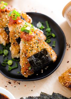 some sushi on a black plate with sesame seeds and green garnishes