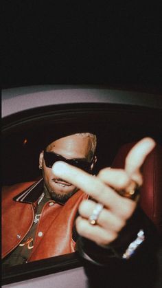 a man in a leather jacket and sunglasses making the v sign with his fingers while sitting in a car